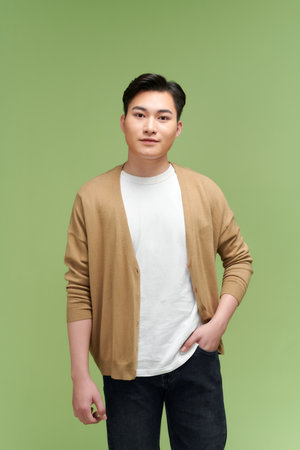 young male with hand in pocket looking at camera against green backgroundの写真素材