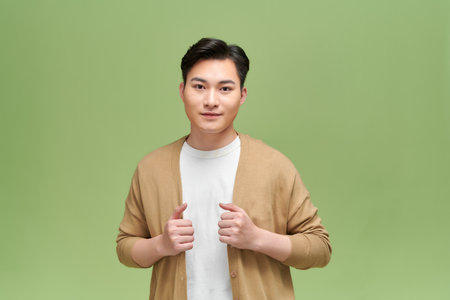 Casual handsome man wearing cardigan smilingon green backgroundの写真素材