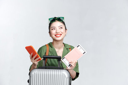 A young woman using cellphone while holding traveling tickets and passport isolatedの写真素材