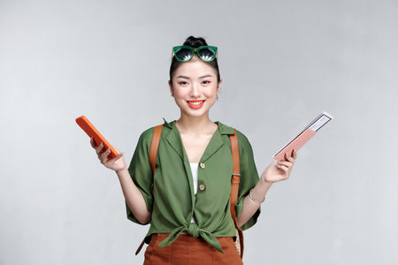 A young woman using cellphone while holding traveling tickets and passport isolatedの写真素材