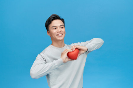 Young man holding red heart over blue backgroundの写真素材