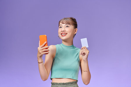 smiling girl holding a credit card and mobile phone online shoppingの写真素材