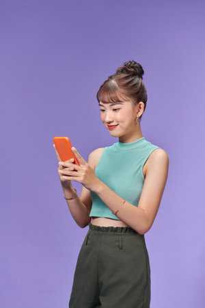 Positive smiling young woman isolated over purple background using mobile phone.の写真素材