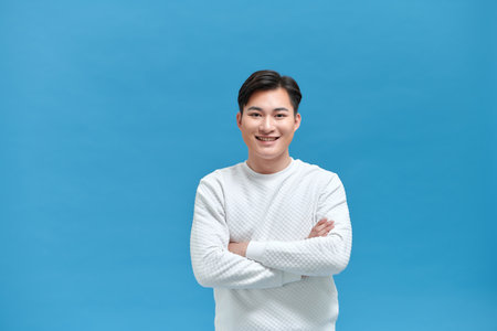 young happy asian man standing with arms crossed over blue wallの写真素材