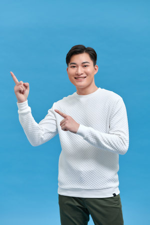 The young man standing on his side pointed his hand to the side with a cheerful expressionの写真素材