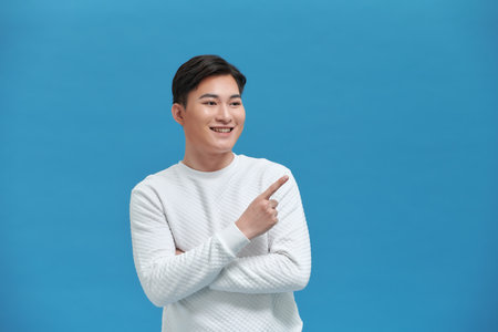 portrait of smiling young handsome Asian man pointing fingers to empty space asideの写真素材