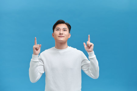 Cheerful young Asian man pointing fingers at copy space, advertisement bannerの写真素材