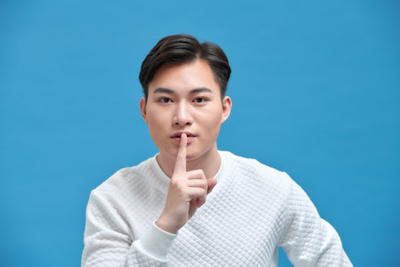 Studio portrait of a young man making a silence gesture, blue backgroundの写真素材