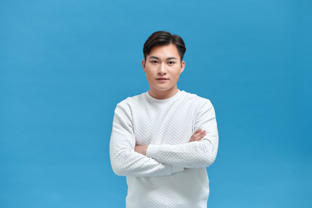 Young man with arms crossed in front of blue wallの写真素材