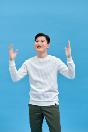Happy guy rejoicing and clenching fists like winner or lucky person, isolated over blue backgroundの写真素材