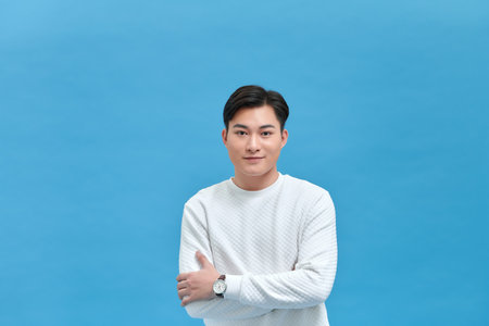 Smiling young Asian man with arms crossed in blue backgroundの写真素材