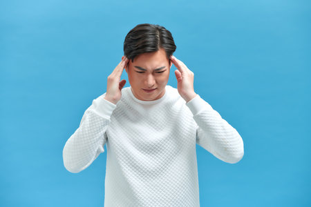 Asian young man looks upset and squeezing their heads with hands from a headacheの写真素材