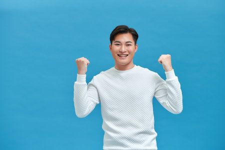 Cheering young man against a blue backgroundの写真素材