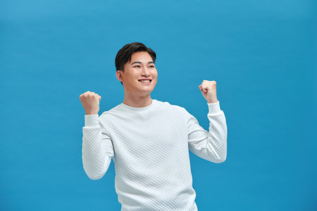 Cheerful excited man standing isolated over blue background, celebrating successの写真素材