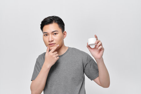Handsome man in a white T-shirt shows cream in his hands and smiles at the cameraの写真素材