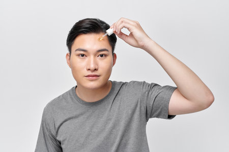 Handsome cheerful man using nourishing serum for his faceの写真素材