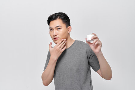 A beautiful smiling man shows the moisturizer that he uses to make his skin smooth and clean from impuritiesの写真素材