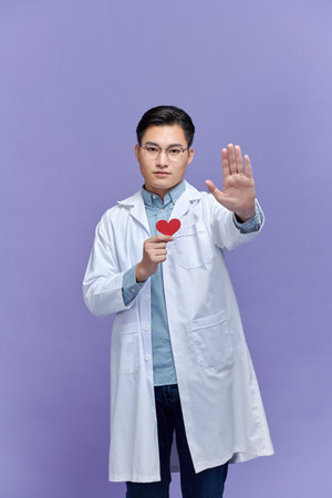 young Asian man doctor holding red heart while looking stressedの写真素材