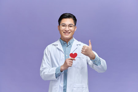Male doctor in uniform hold red heart and show OK or approval sign with thumb upの写真素材