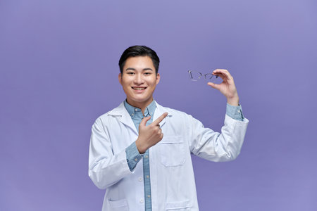 Happy asian ophthalmologist doctor holding glasses, recommending to improve eyesight, looking at cameraの写真素材