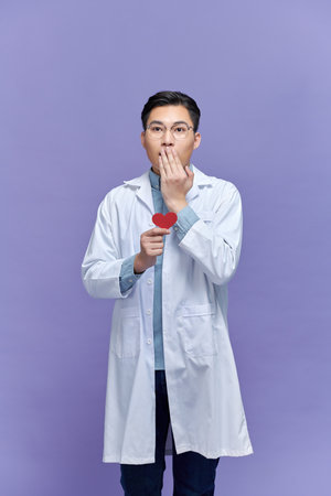 cardiologist doctor man holding red heart, cover mouth with hand secret conceptの写真素材