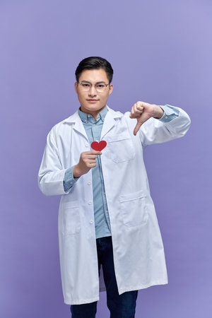 cardiologist doctor woman holding red heart, negative sign showing dislike with thumbs down, rejection conceptの写真素材