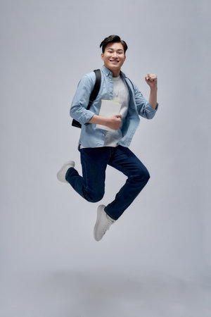 Full length shot of a tall guy holding books and jumping isolated on white backgroundの写真素材