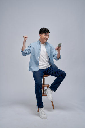 Young Asian man play game on mobile phone application and raising his arm up with celebrating successの写真素材