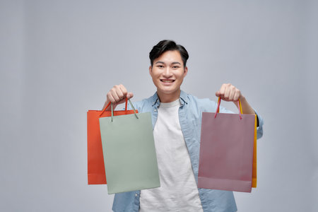 Portrait of a smiling man holding shopping bag over gray background and looking at cameraの写真素材