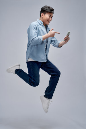 Excited man holding and pointing finger at his cell phone while jumpingの写真素材
