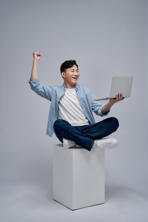 Full length photo of young excited funny guy fists up sitting platform use laptop on white backgroundの写真素材