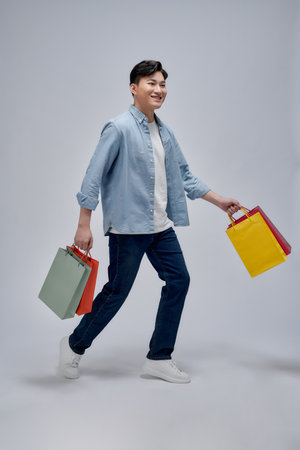 happy young man holding colorful paper bags while looking at cameraの写真素材