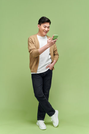 Attractive man chatting or typing text message using cell phone isolated over green backgroundの写真素材