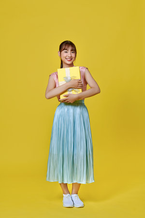 Full length portrait of a happy woman holding gifts isolated on a  yellow backgroundの写真素材