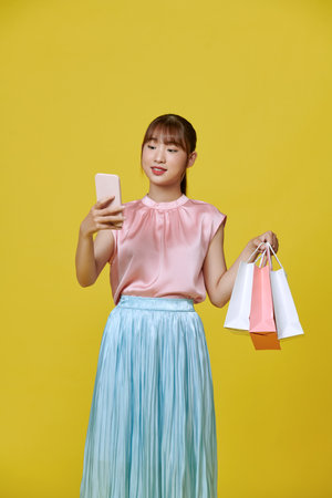 Young asian woman on yellow background, shoppingの写真素材