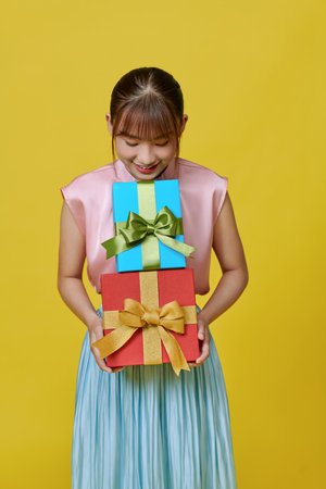 Pretty woman hands many presents wrapped in colorful paper, isolated on yellowの写真素材