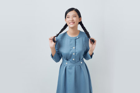 young female playing with her braids looking away isolated on whiteの写真素材