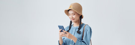 Studio portrait of happy smiling young female tourist holding phone, isolated on yellow backgroundの写真素材