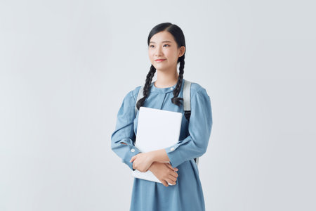 Cheerful attractive asian girl with backpack making notes in notebook isolated on a white backgroundの写真素材