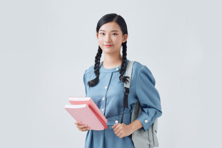 Cheerful attractive asian girl with backpack making notes in notebook isolated on a white backgroundの写真素材