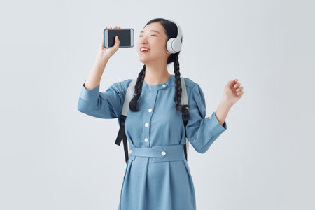 Excited emotional asian woman singing her favorite song, using smartphone as microphoneの写真素材