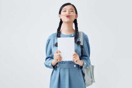 Portrait of funny female student keeping pencil between nose and lips as moustacheの写真素材