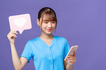 Photo portrait happy woman showing heart icon keeping mobile phone isolated on purple backgroundの写真素材