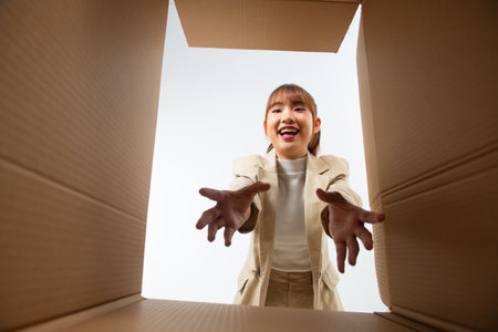 Excited asian woman unpacking, opening carton box and trying to get something, view from the insideの写真素材