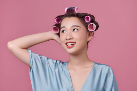 Beautiful young woman in silk dress with hair curlers on pink background. Space for textの写真素材
