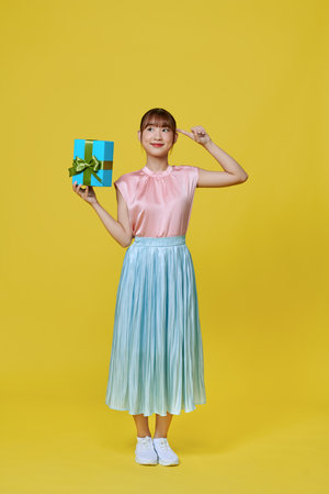 Full size photo of satisfied ecstatic woman presenting gift box isolated on yellow backgroundの写真素材