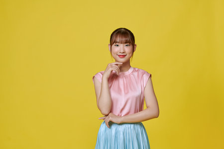 Smiling beautiful attractive young woman in silk casual dress posing  isolated on yellow backgroundの写真素材