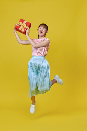 Full size photo of satisfied ecstatic woman presenting gift box isolated on yellow backgroundの写真素材