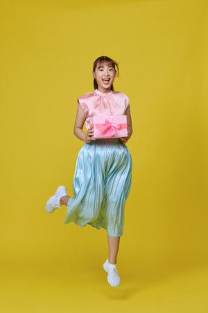 Full size profile photo of pretty  lady jump with present isolated on yellow backgroundの写真素材
