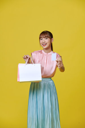 Young Asian businesswoman holding shopping bags posing on yellow backgroundの写真素材